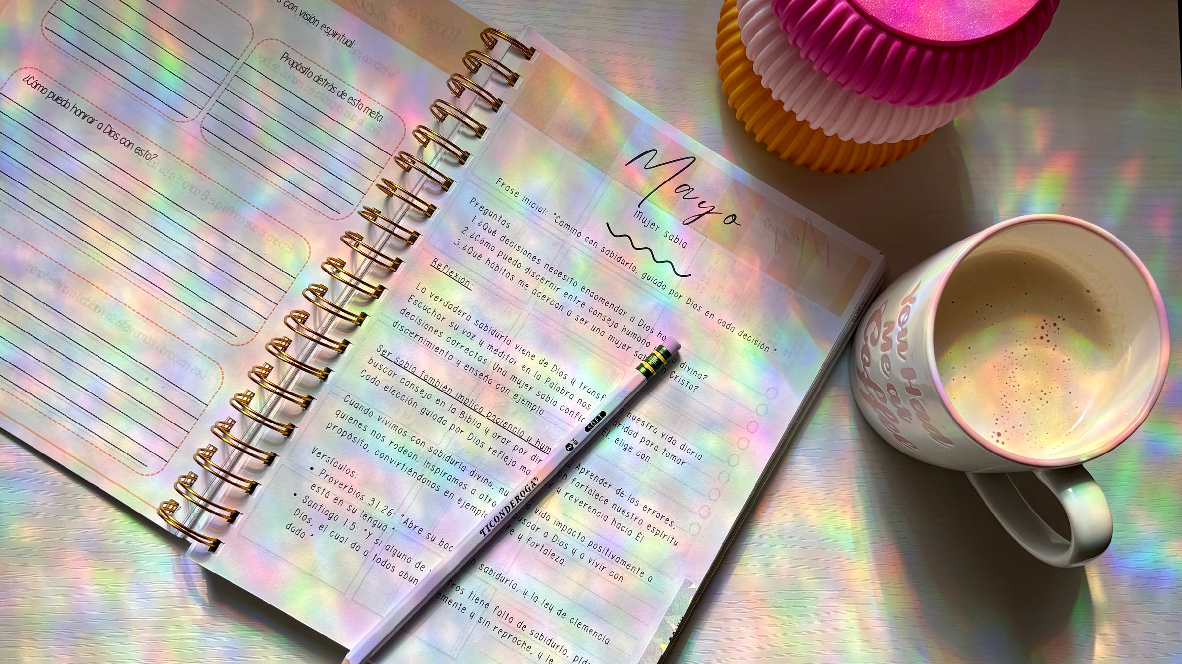 Open planner with holographic cover, pen, and coffee cup on a reflective surface